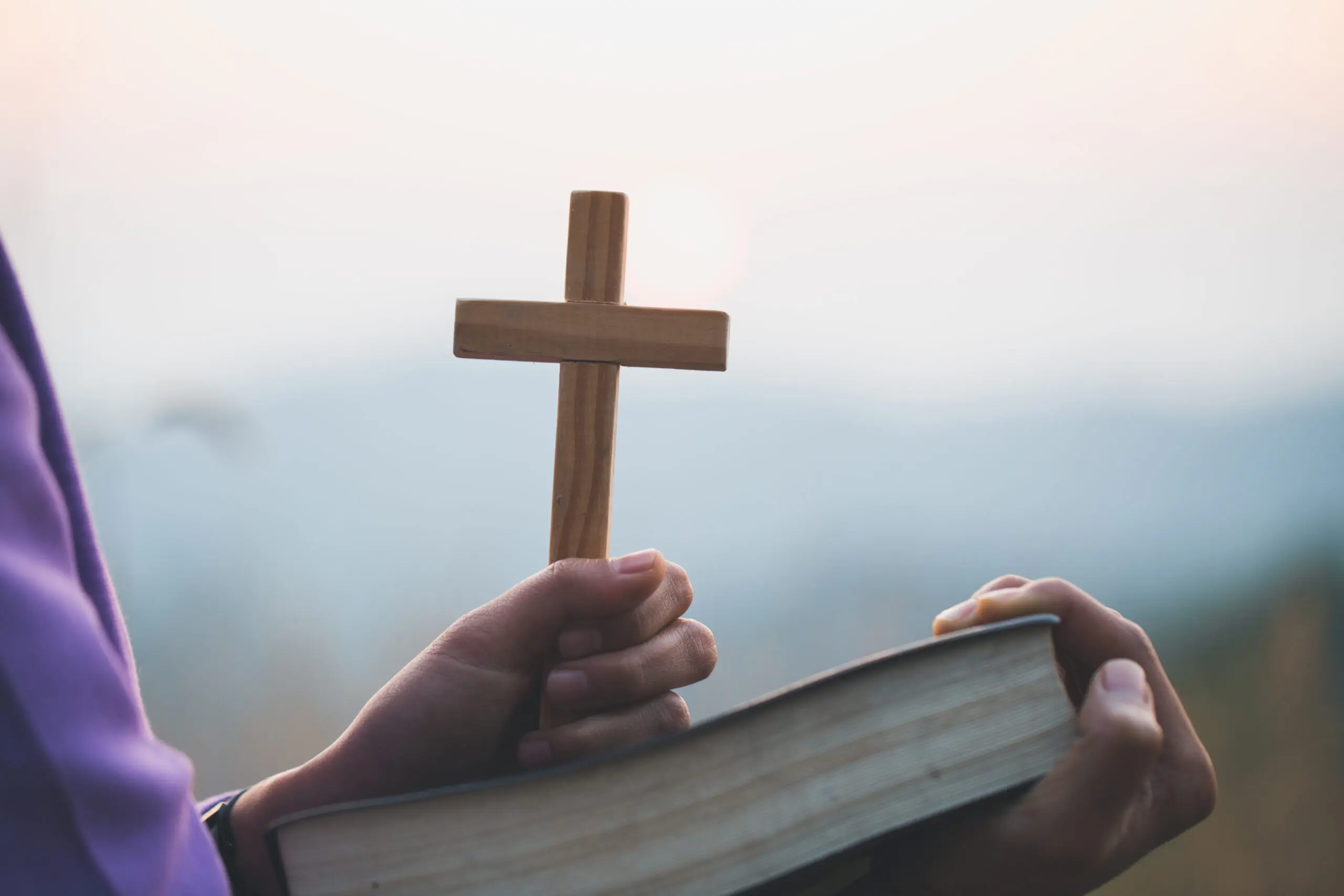 Person holding cross and open book.