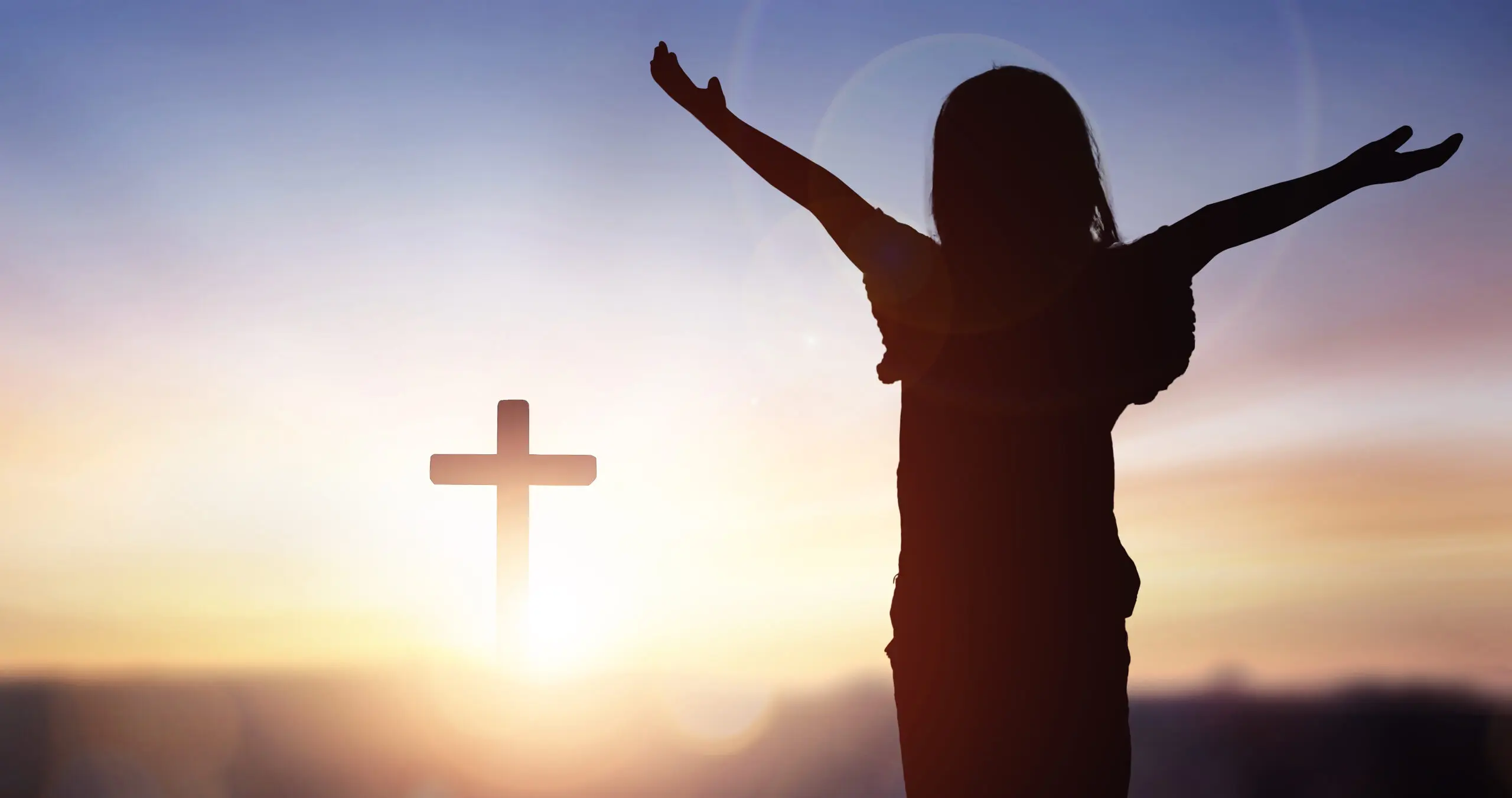 Silhouette of person with cross at sunset.