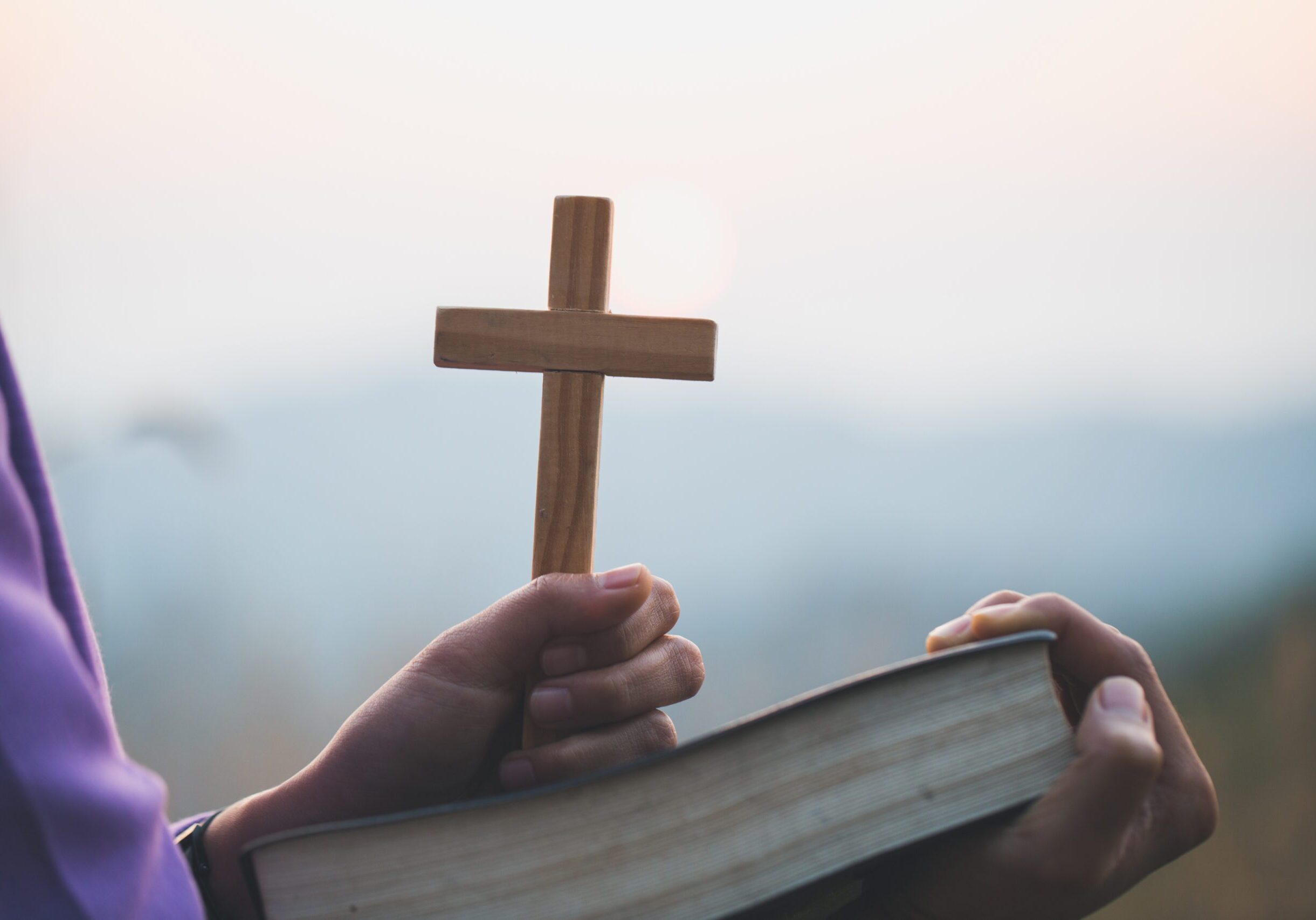 Person holding cross and open book.