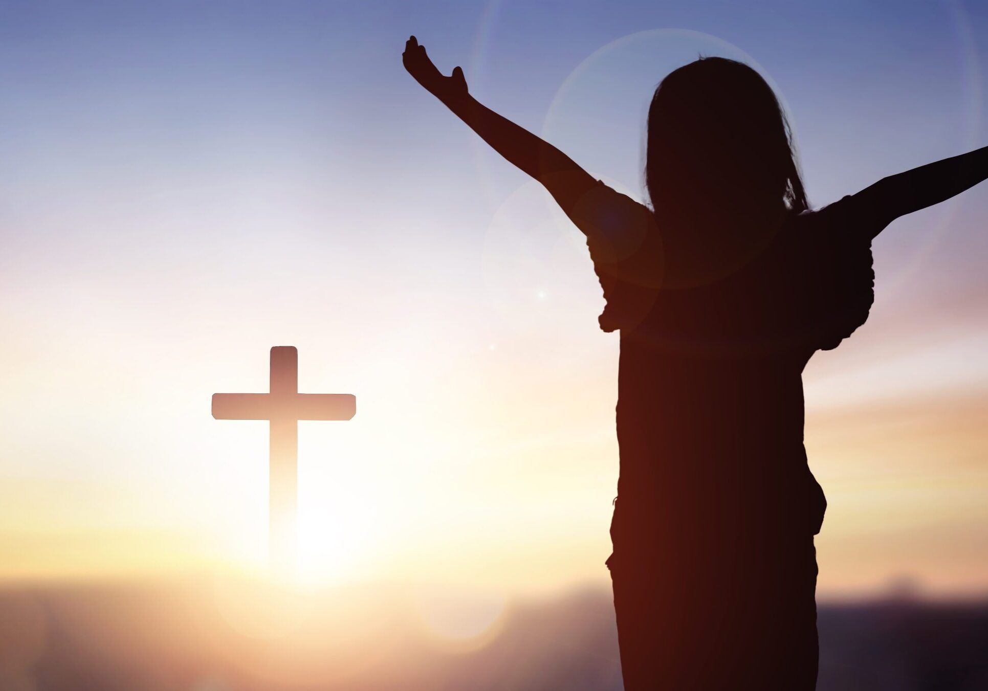 Silhouette of person with cross at sunset.